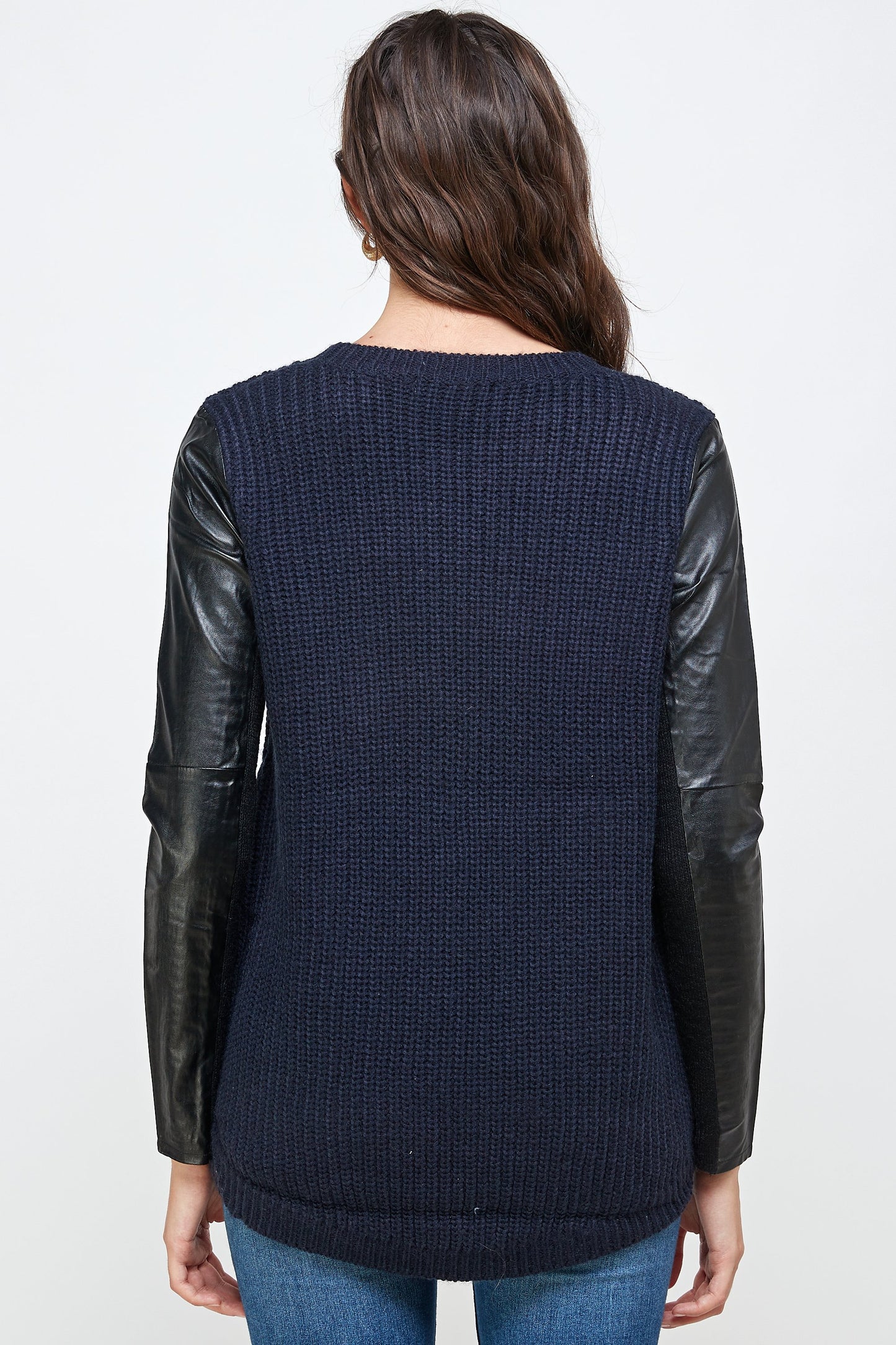 A back view of an Indigo Arrowwood Vegan Leather Sweater High Low Top reveals a stylish combination of a navy knit with black vegan leather sleeves, highlighting chic and animal-friendly fashion.