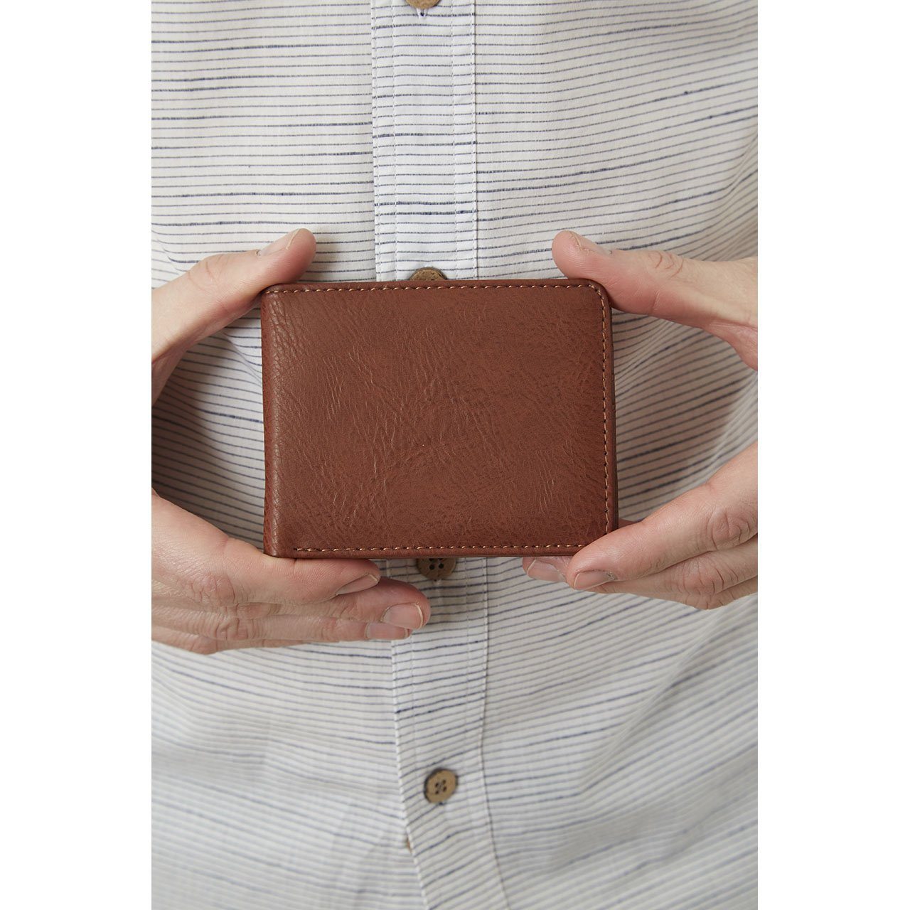 A conscious consumer in a striped shirt holds a closed Yellow Florence Easy Vegan Leather Bi-Fold Wallet with both hands.