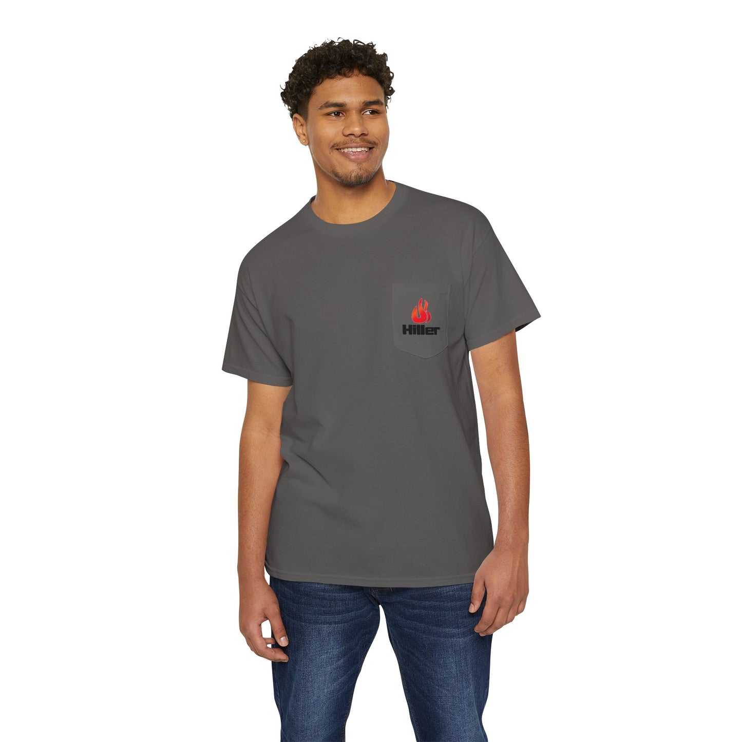 A man in blue jeans smiles, wearing a gray Printify Unisex Heavy Cotton Pocket Tee with a flame logo and "Hiller" text—ideal for casual outings or outdoor adventures.