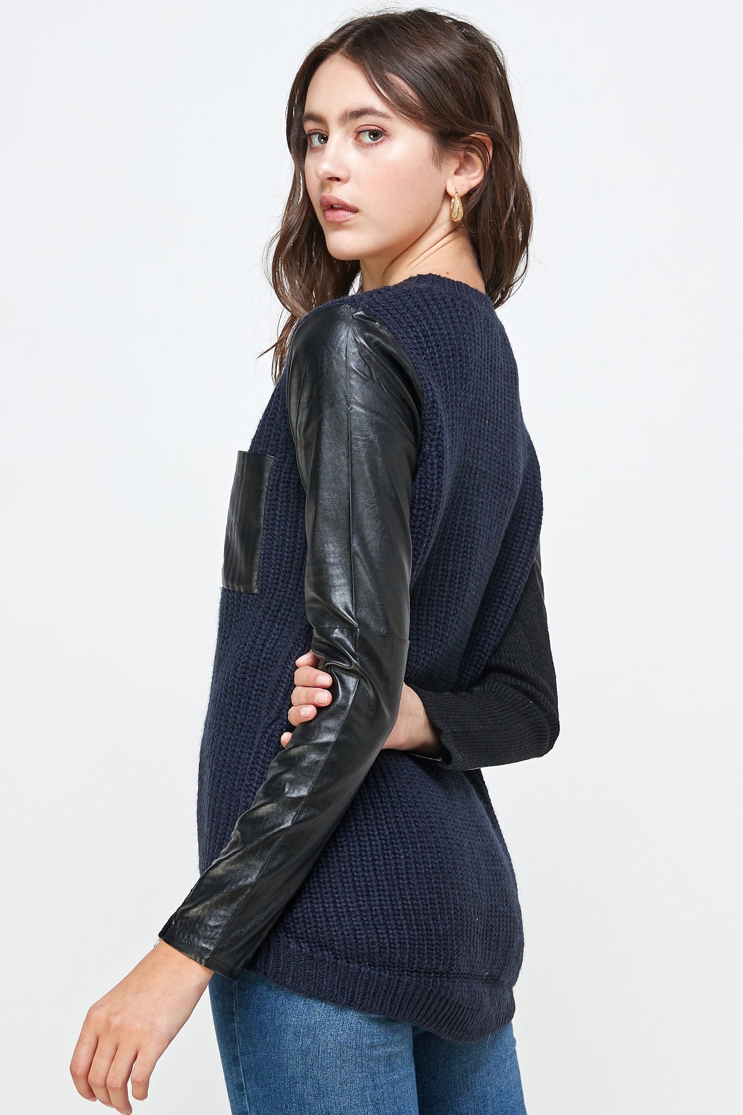 Wearing the Vegan Leather Sweater High Low Top by Indigo Arrowwood, featuring a navy vegan body and black leather sleeves, paired with jeans against a plain backdrop, embodies animal-friendly fashion.