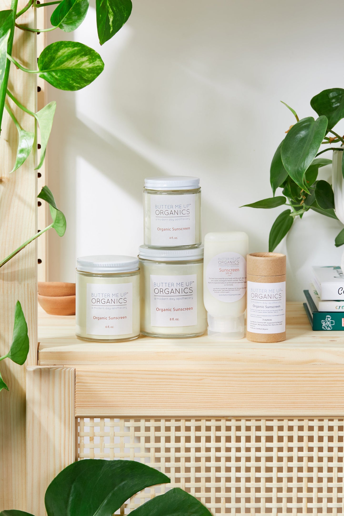 A shelf full of candles and plants on a shelf, with White Smokey Non-Nano Zinc Oxide SPF 45 Sunscreen amongst them.