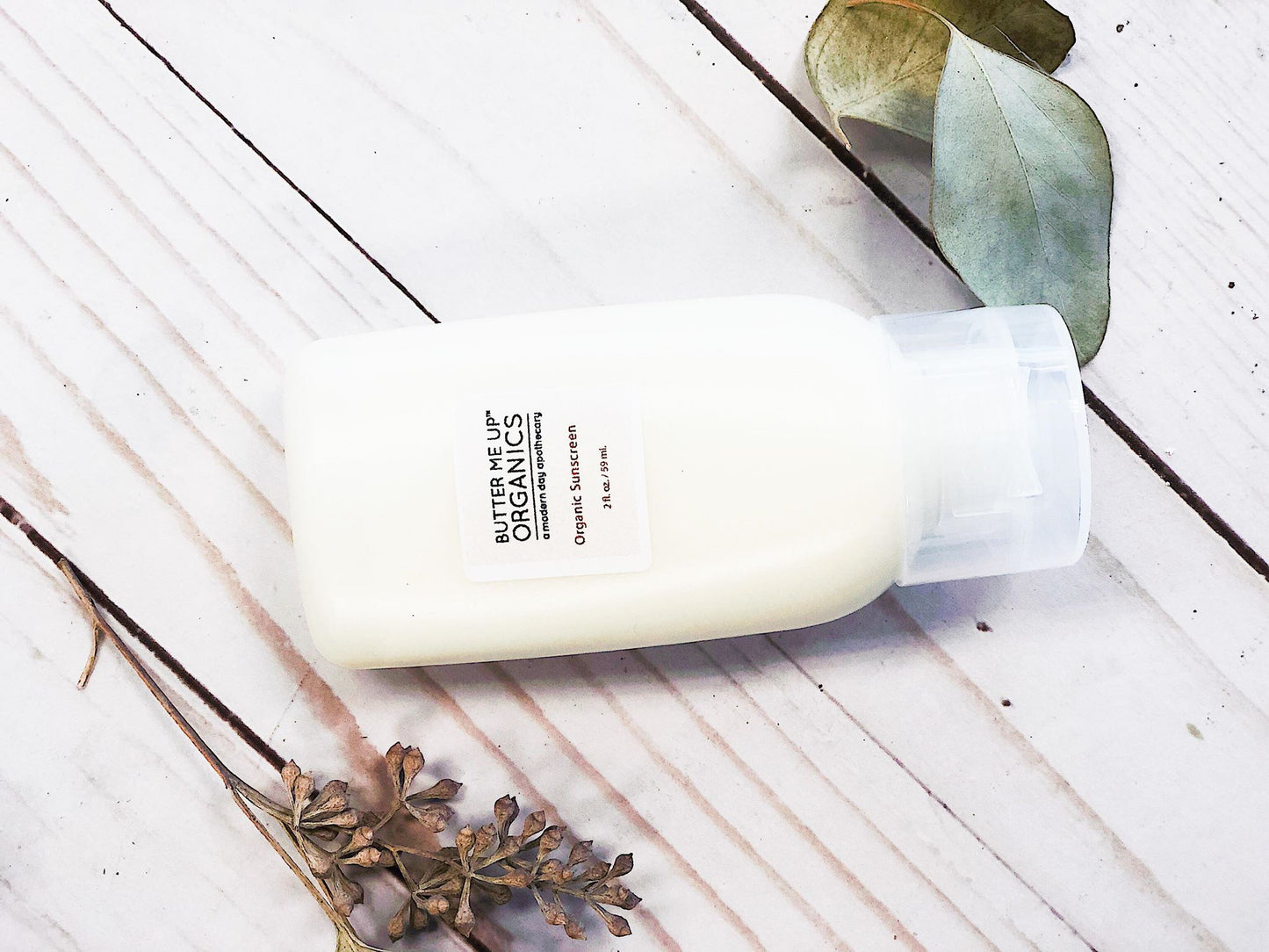 A bottle of Natural Organic Sunscreen with eucalyptus leaves and SPF 45 Sunscreen by White Smokey on a wooden table.