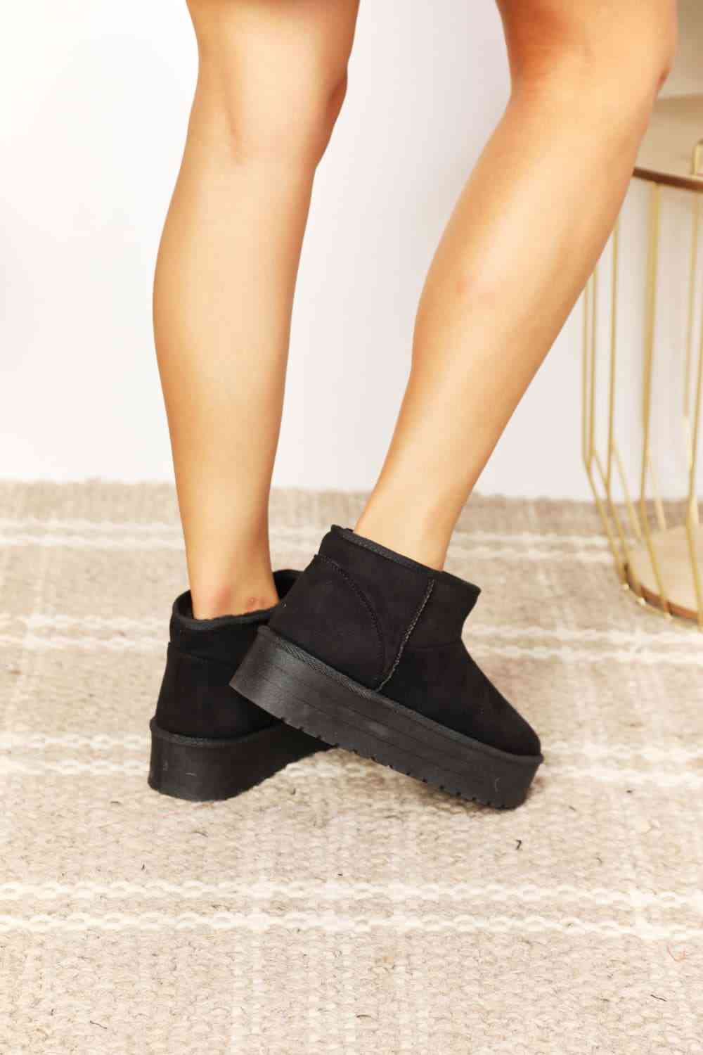 Person wearing Legend Women's Fleece Lined Chunky Platform Mini Boots by Trendsi standing on a textured rug.