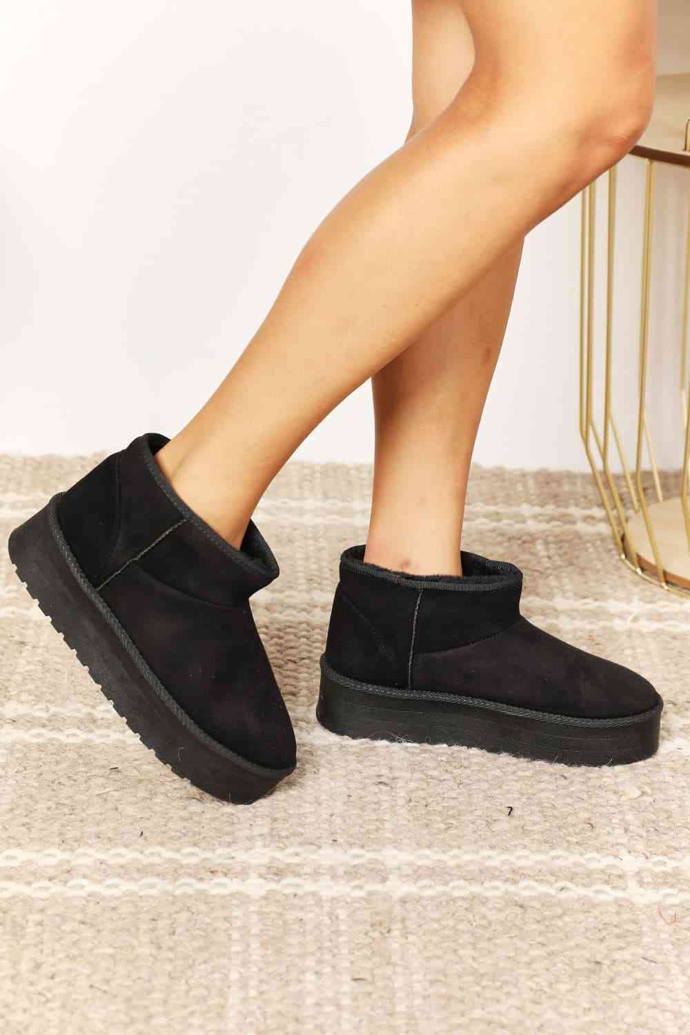 A person wearing Trendsi's Legend Women's Fleece Lined Chunky Platform Mini Boots stands on a beige woven rug.
