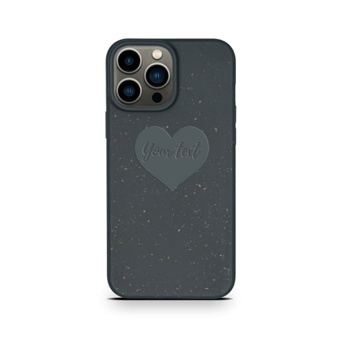 A Tan Lily biodegradable personalized iPhone case in black with a speckled design and a heart-shaped space for custom text, fitted on a phone with three camera lenses.