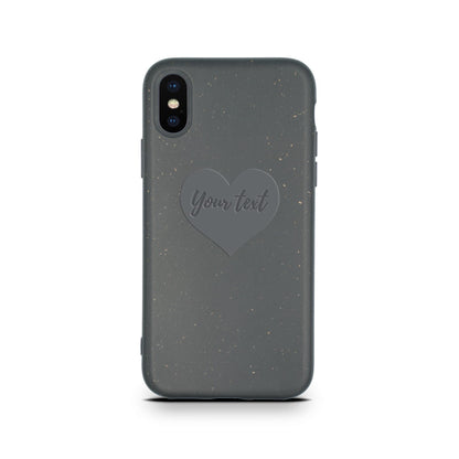 A Biodegradable Personalized Iphone Case - Black from Tan Lily in a black speckled, eco-friendly phone case with a customizable heart-shaped text area saying "Your text" on a white background.