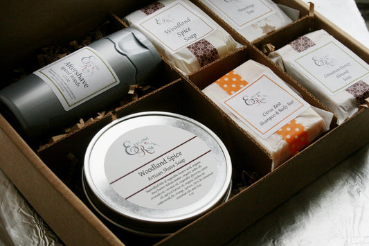 An open gift box containing the Maroon Oliver Just for Him Gift Set, Natural Bath Gift for Men, including artisan shave soaps and moisturizers, labeled with elegant branding.