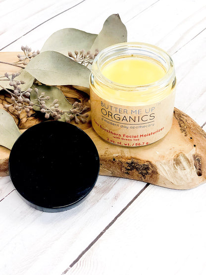 Jar of White Smokey Acne Bundle and Organic Skincare Moisturizer with the lid off, displayed on a wooden surface with decorative leaves.