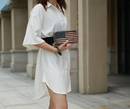 A woman in a white dress holding an Uriel Vegan Leather Women's FLAG Wristlet Wallet made by Pink Orpheus.