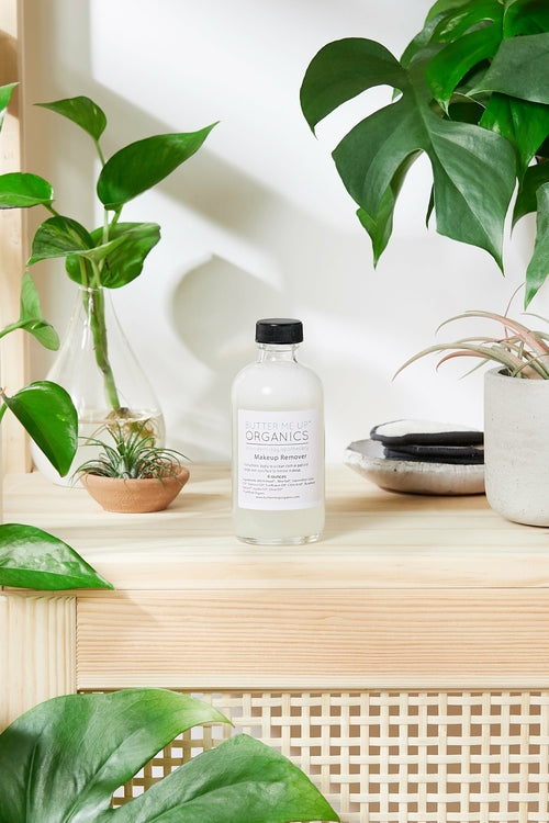 An efficient, non-toxic White Smokey Organic Makeup Remover bottle sits on a shelf next to a potted plant.