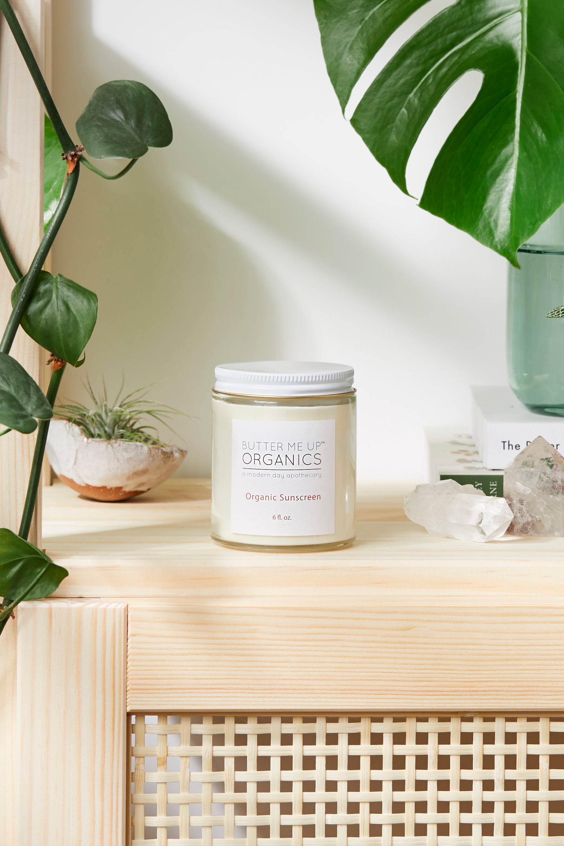 A plant sits next to a wooden shelf where a Natural Organic Sunscreen from the brand White Smokey flickers, providing a warm glow.