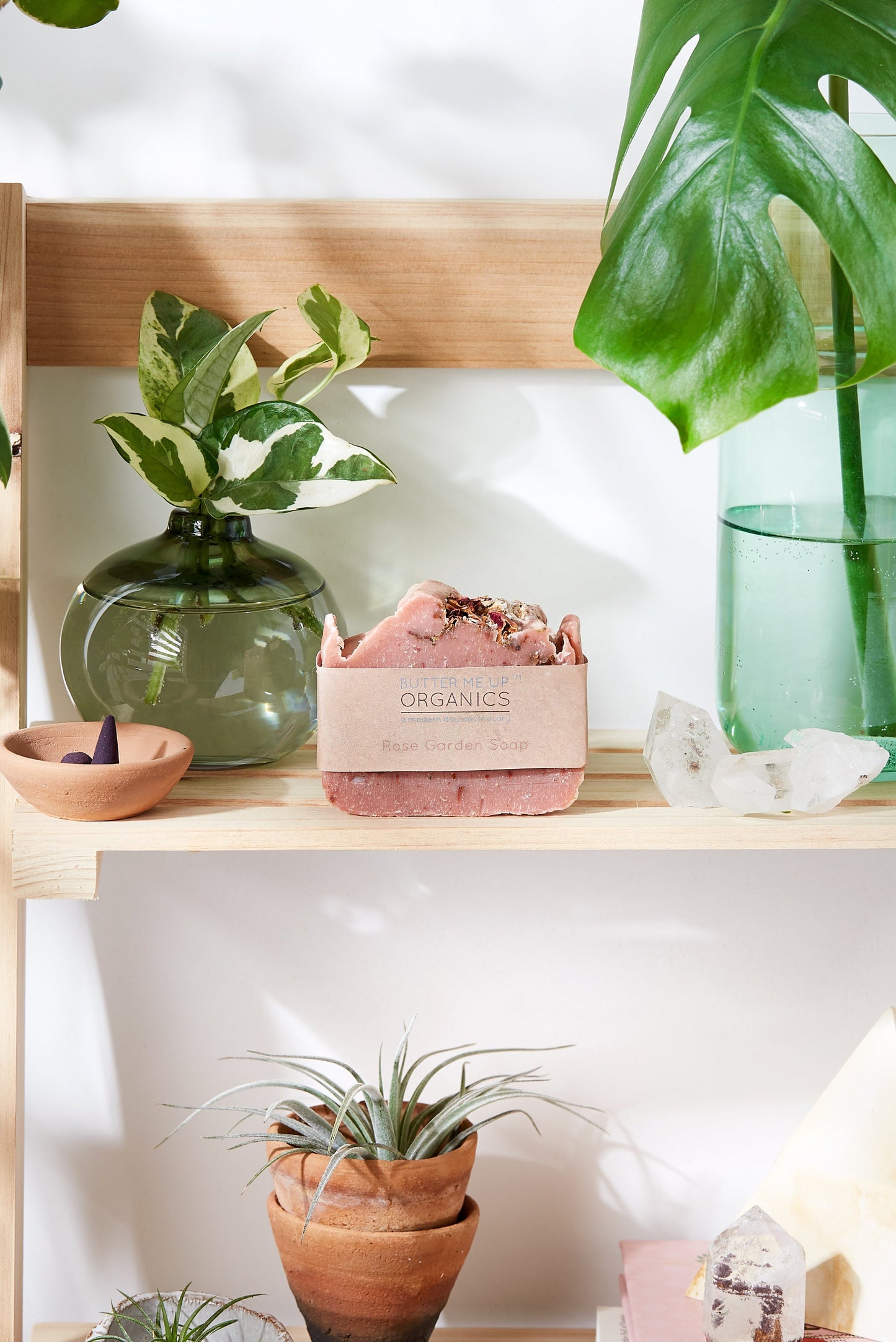 A wooden shelf adorned with natural plants and fragrant soaps, including White Smokey's Rose Garden Organic Soap, Vegan Soap, and Palm Free.