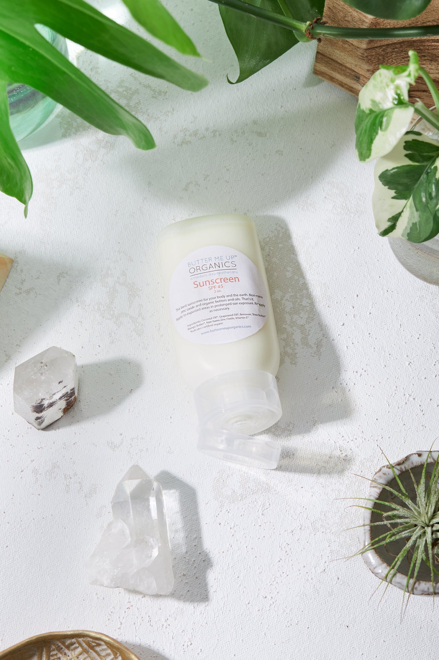 A white table with plants and a bottle of White Smokey SPF 45 Sunscreen.