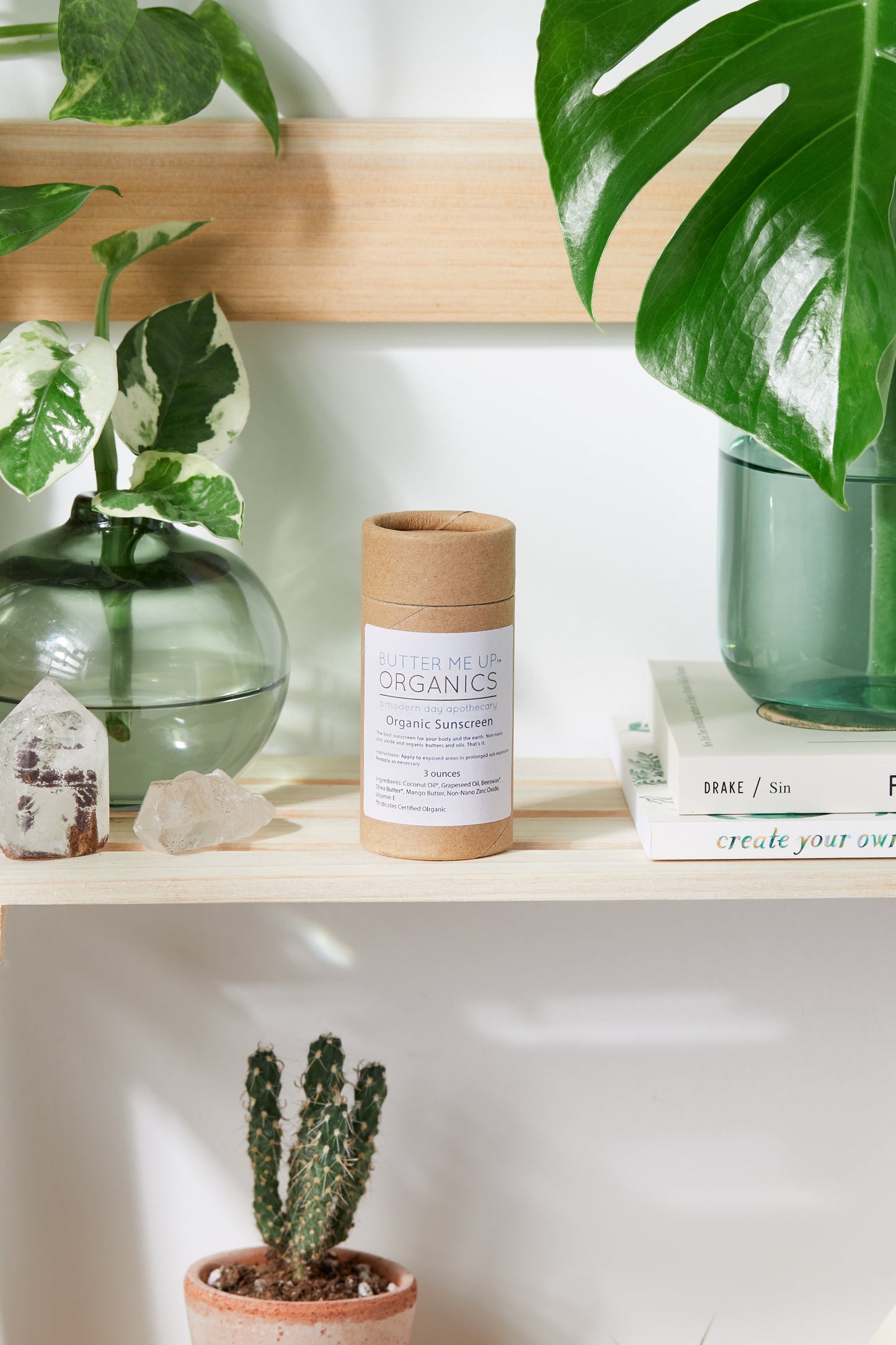 A shelf with books, plants, and a candle featuring White Smokey SPF 45 Sunscreen to protect against harmful sun rays.