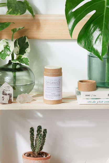 A shelf with books, plants, and a candle featuring White Smokey's zinc oxide-based SPF 45 Natural Organic Sunscreen.