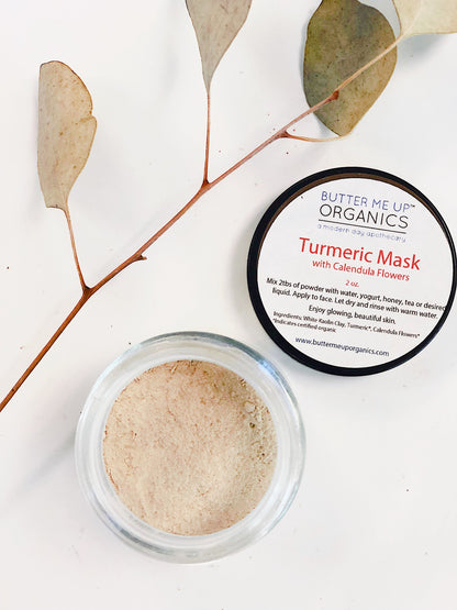 A jar of White Smokey turmeric mask with its lid and dry eucalyptus leaves on a white surface.