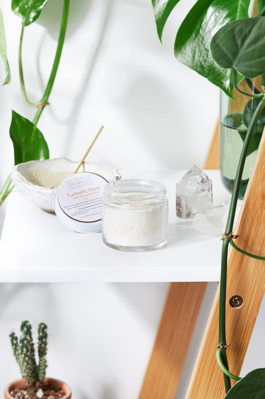 A jar of White Smokey Turmeric Mask on a wooden shelf surrounded by plants and calming natural decor.