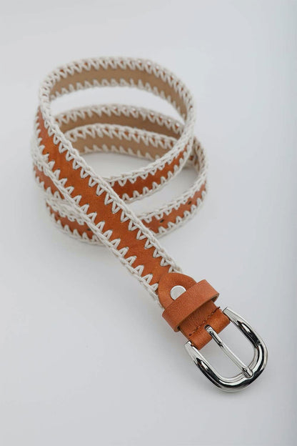 A brown Periwinkle Aether Crochet Vegan Leather Belt with white zigzag stitching along the edges, featuring a silver buckle, coiled neatly on a white background.
