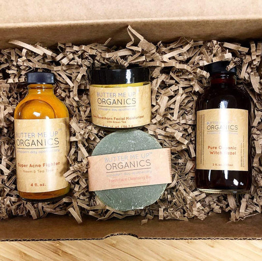 A set of White Smokey's Acne Bundle organic skincare products, including a French Green Clay Face wash, acne fighter oil, cleansing bar, and witch hazel, packaged in a cardboard box with eco-friendly materials.