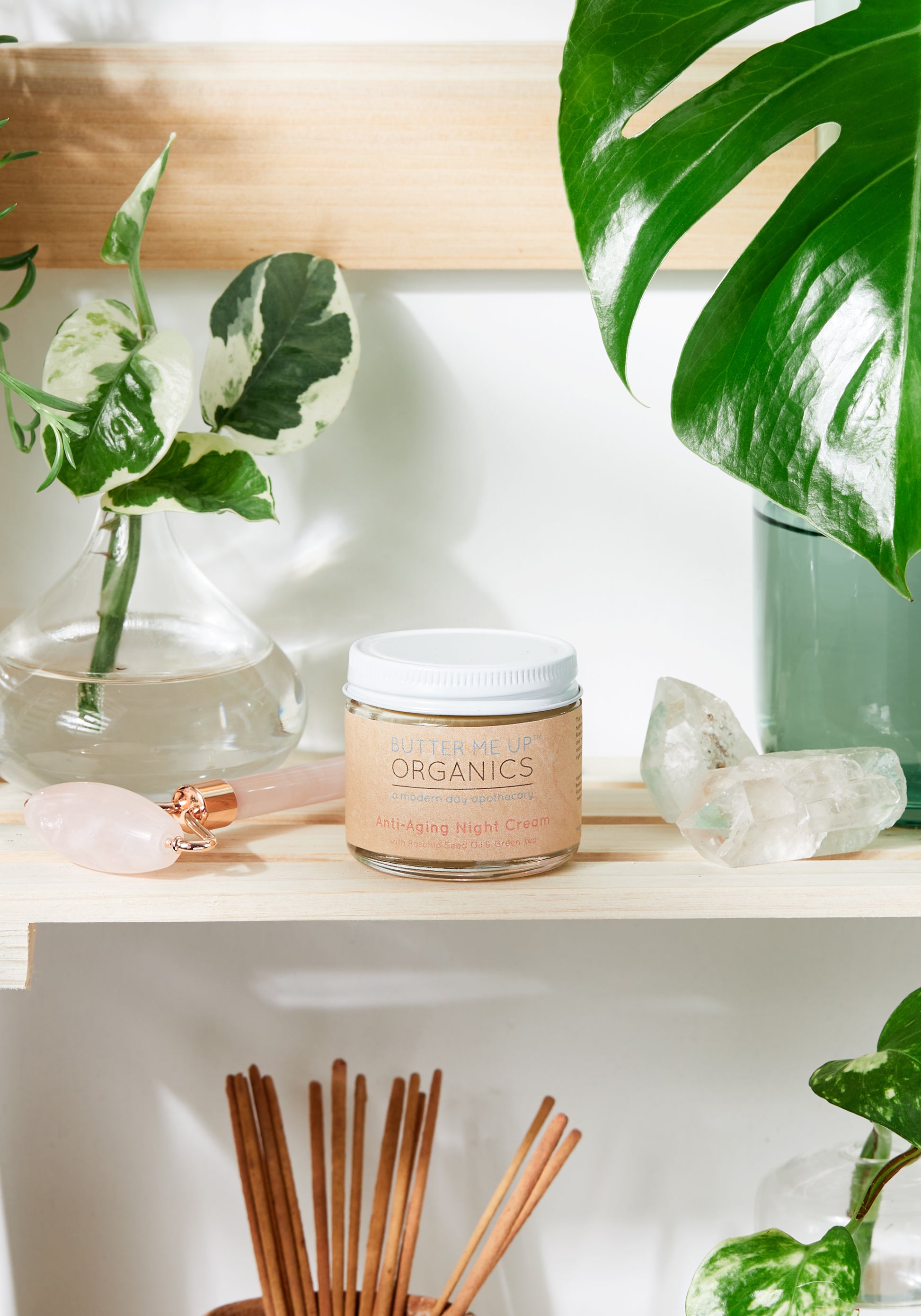 A jar of White Smokey Anti Aging Night Cream Face Moisturizer Organic surrounded by houseplants, crystals, and incense sticks on a wooden shelf.