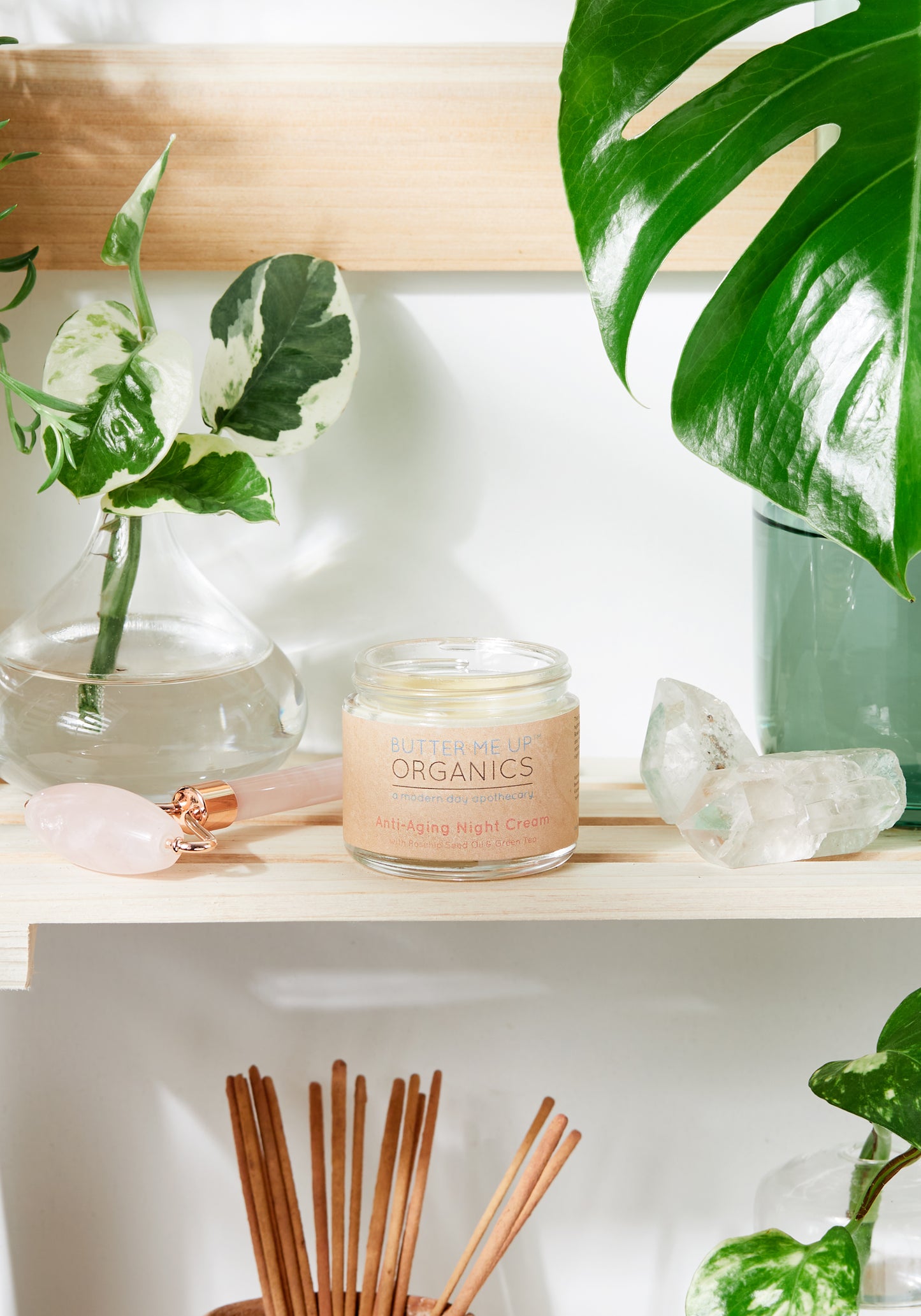 A jar of "White Smokey Anti Aging Night Cream Face Moisturizer Organic" on a shelf surrounded by green plants, crystals, and incense sticks, conveying a serene spa-like atmosphere. This anti-wrinkle cream is formulated with all-natural ingredients.
