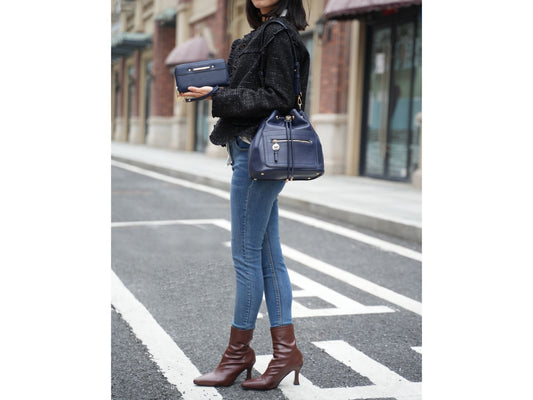 A woman in jeans carrying a stylish Black Orpheus Larissa Vegan Leather Women’s Bucket Bag with Wallet with an adjustable strap made of high-quality vegan leather, standing on the street.