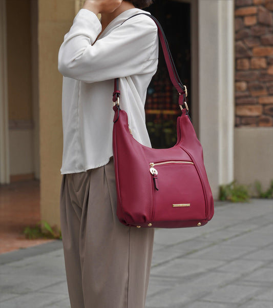 A fashion-forward woman holding a Lavinia Vegan Leather Women’s Shoulder Bag with gold-tone embellishments on a sidewalk.
