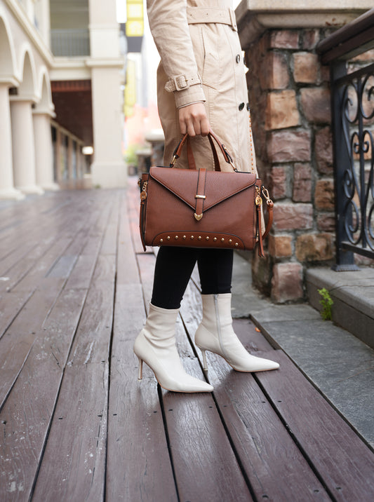 A woman in a trench coat and white boots holding a Pink Orpheus Angela Vegan Leather Women’s Satchel Bag.