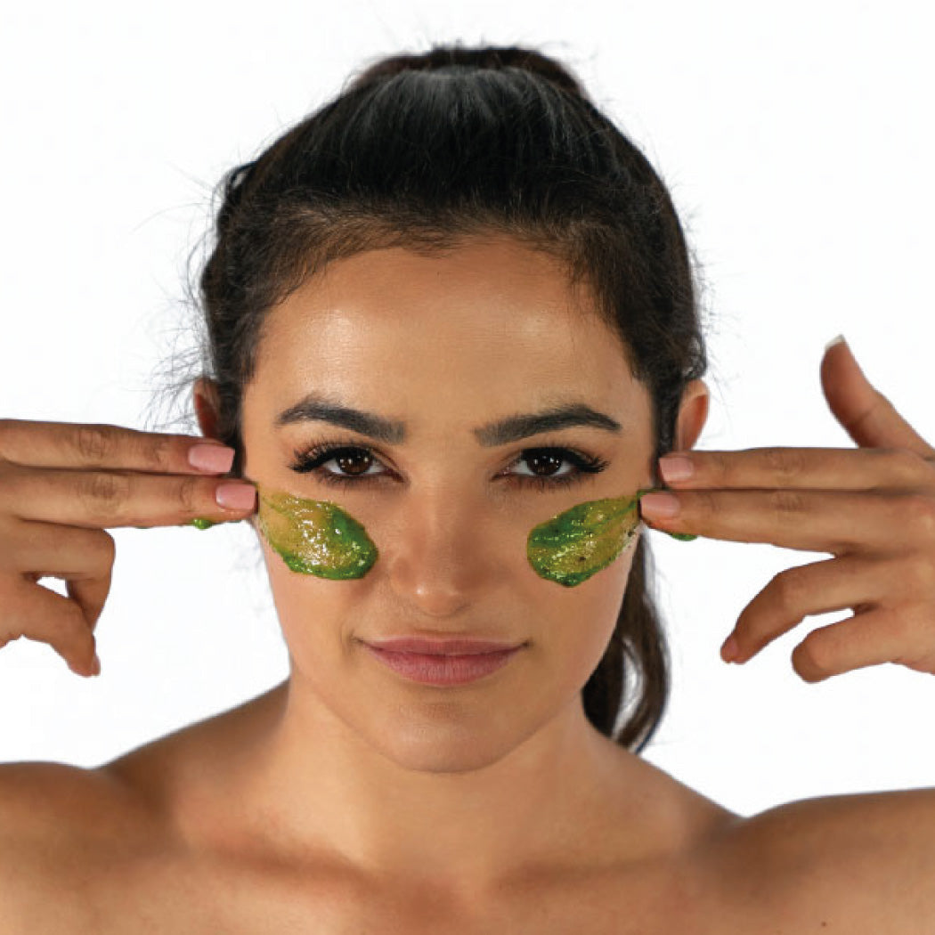 Woman applying Cyan Ares Detoxifying Exfoliating Mask under her eyes.