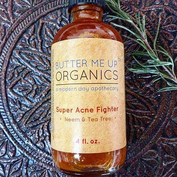 A 4 fl. oz. bottle of "White Smokey Super Acne Fighter," an acne-fighting serum with neem and tea tree organic oils, placed on a textured surface next to a sprig of greenery.