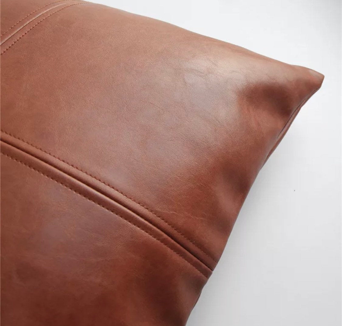 A close-up of a brown Magenta Charlie Vegan Leather Pillow Cover with visible stitching and smooth texture on a white background.