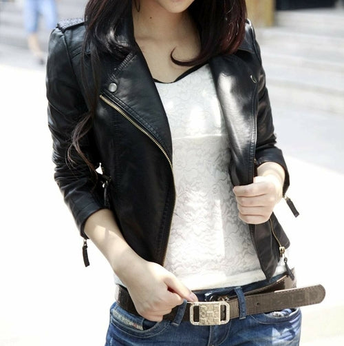 A person is wearing a black **Womens Cropped Vegan Leather Jacket** by **Yellow Pandora** over a white lace top, paired with blue jeans and a brown belt. The person is holding the belt.