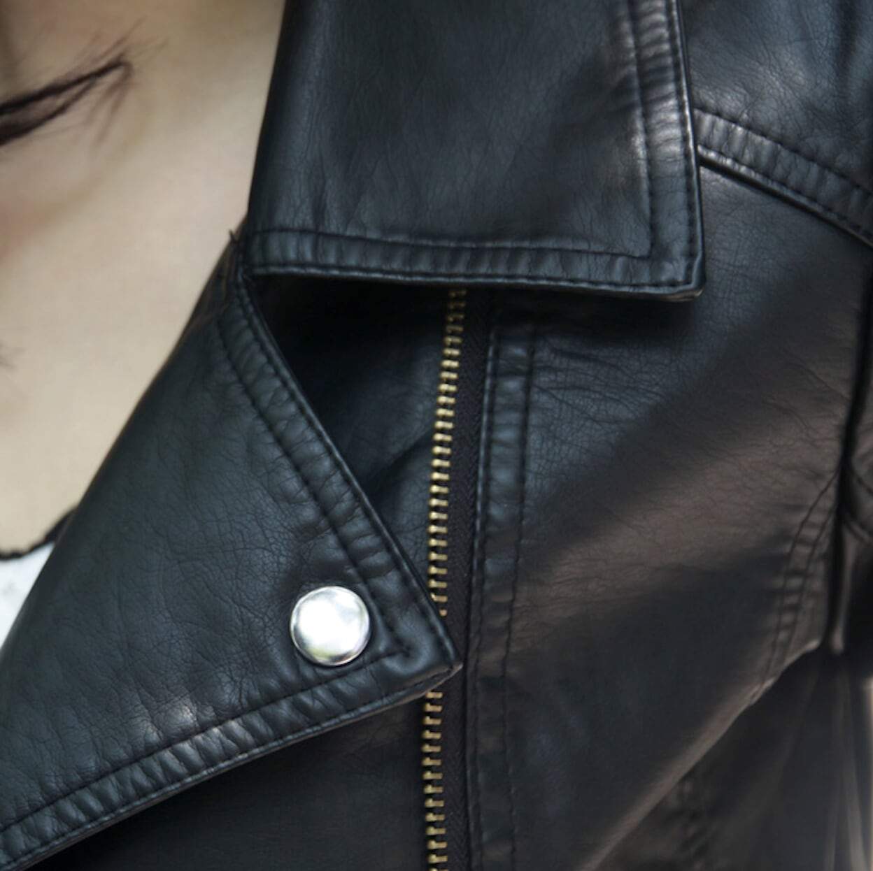 Close-up of a person wearing a Yellow Pandora Womens Cropped Vegan Leather Jacket, featuring a visible silver zipper and button detail.