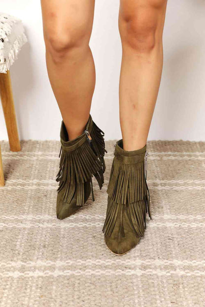 A person wearing Trendsi's Legend Women's Tassel Wedge Heel Ankle Booties stands on a carpeted floor, showcasing just the lower legs and feet.