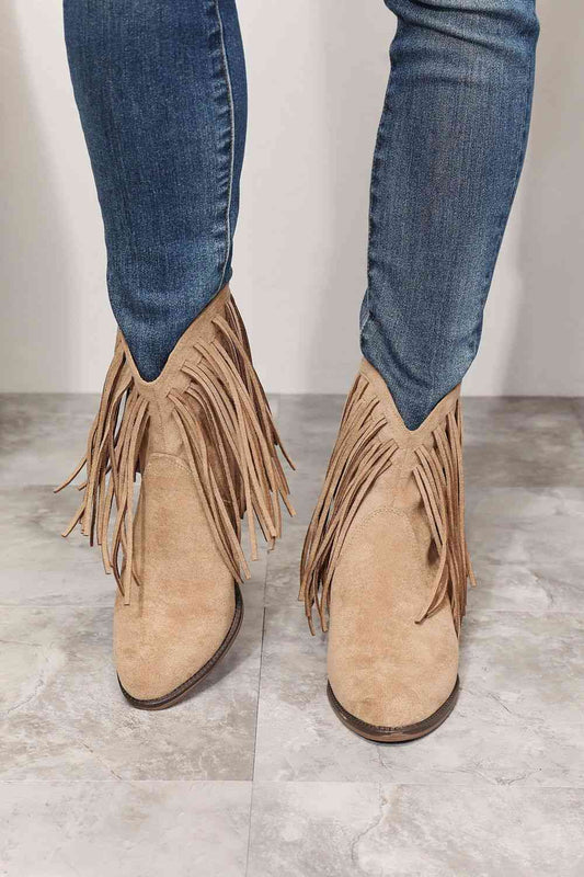 A person standing on a tiled floor wearing blue jeans and tan Trendsi Legend Women's Fringe Cowboy Western Ankle Boots.