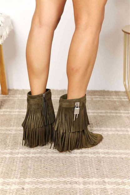 A person wearing Trendsi's Legend Women's Tassel Wedge Heel Ankle Booties stands on a textured rug, with a partial view of a wooden stool in the background.