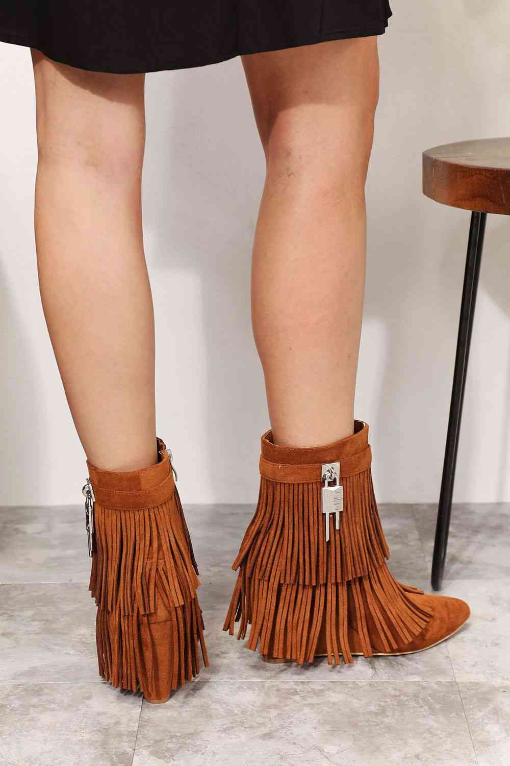 A woman's feet in a pair of Legend Women's Tassel Wedge Heel Ankle Booties by Trendsi with an open shank design, made with vegan suede.